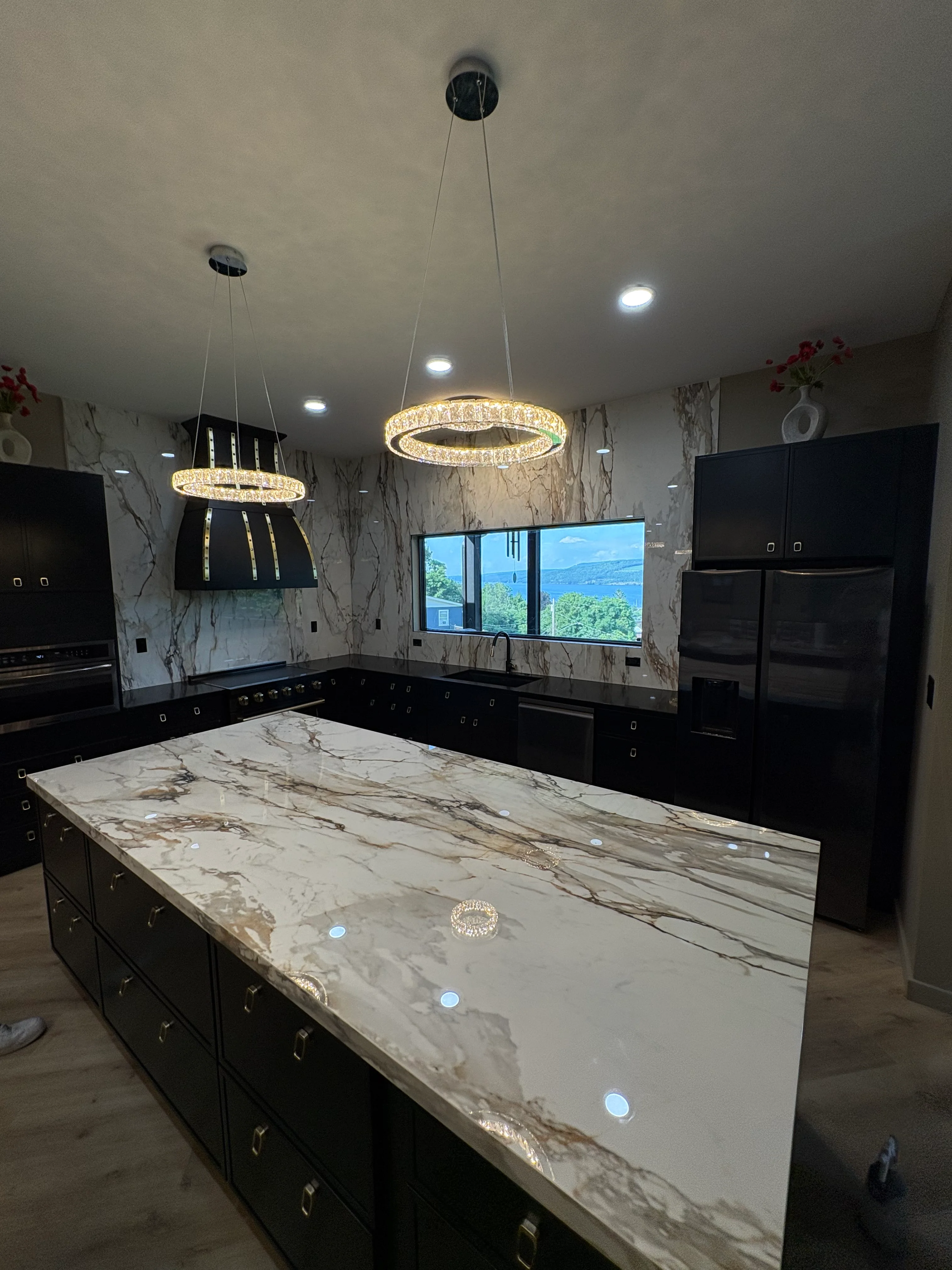 Marble waterfall island countertop with black cabinetry and crystal pendant lighting in modern kitchen