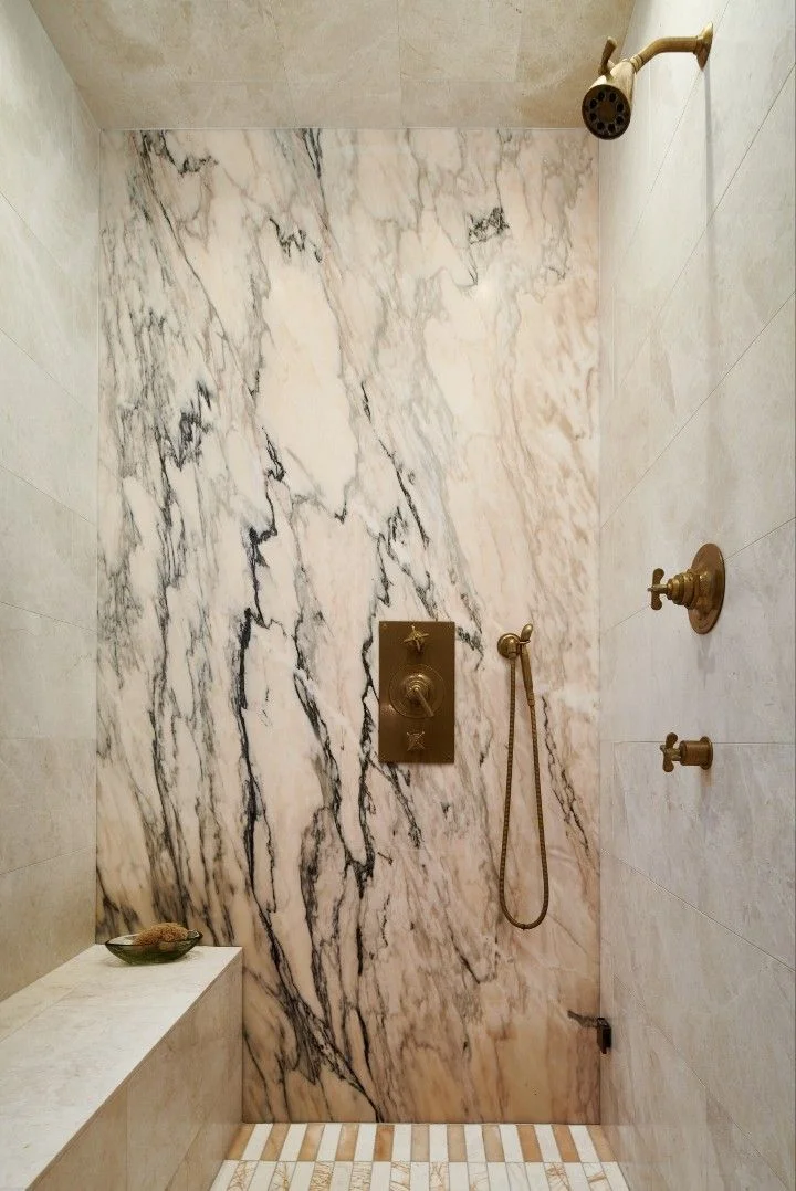 Marble shower with veined accent wall, brass fixtures, and marble bench seat