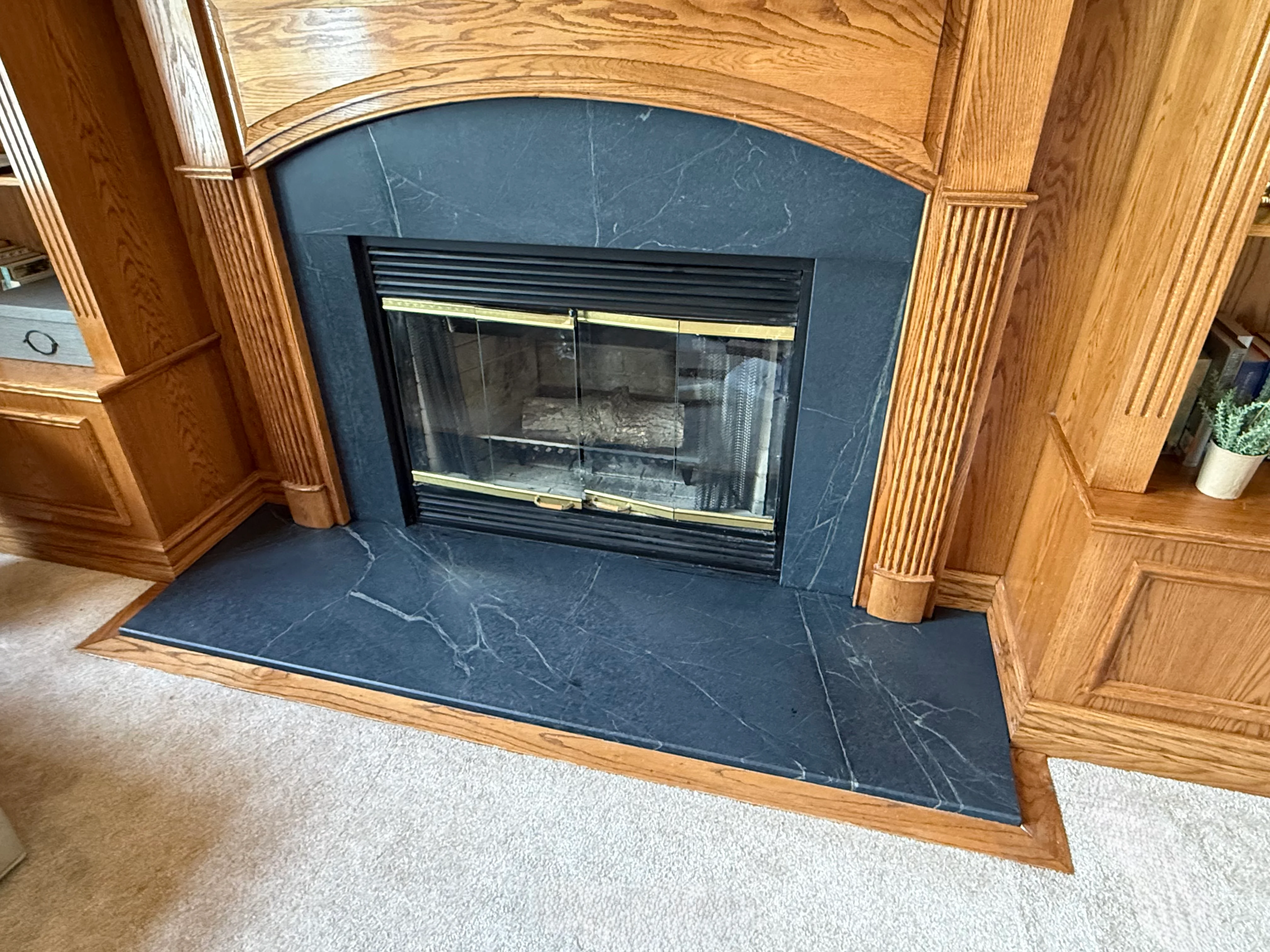 Dark slate fireplace surround and hearth with arched opening and brass accents