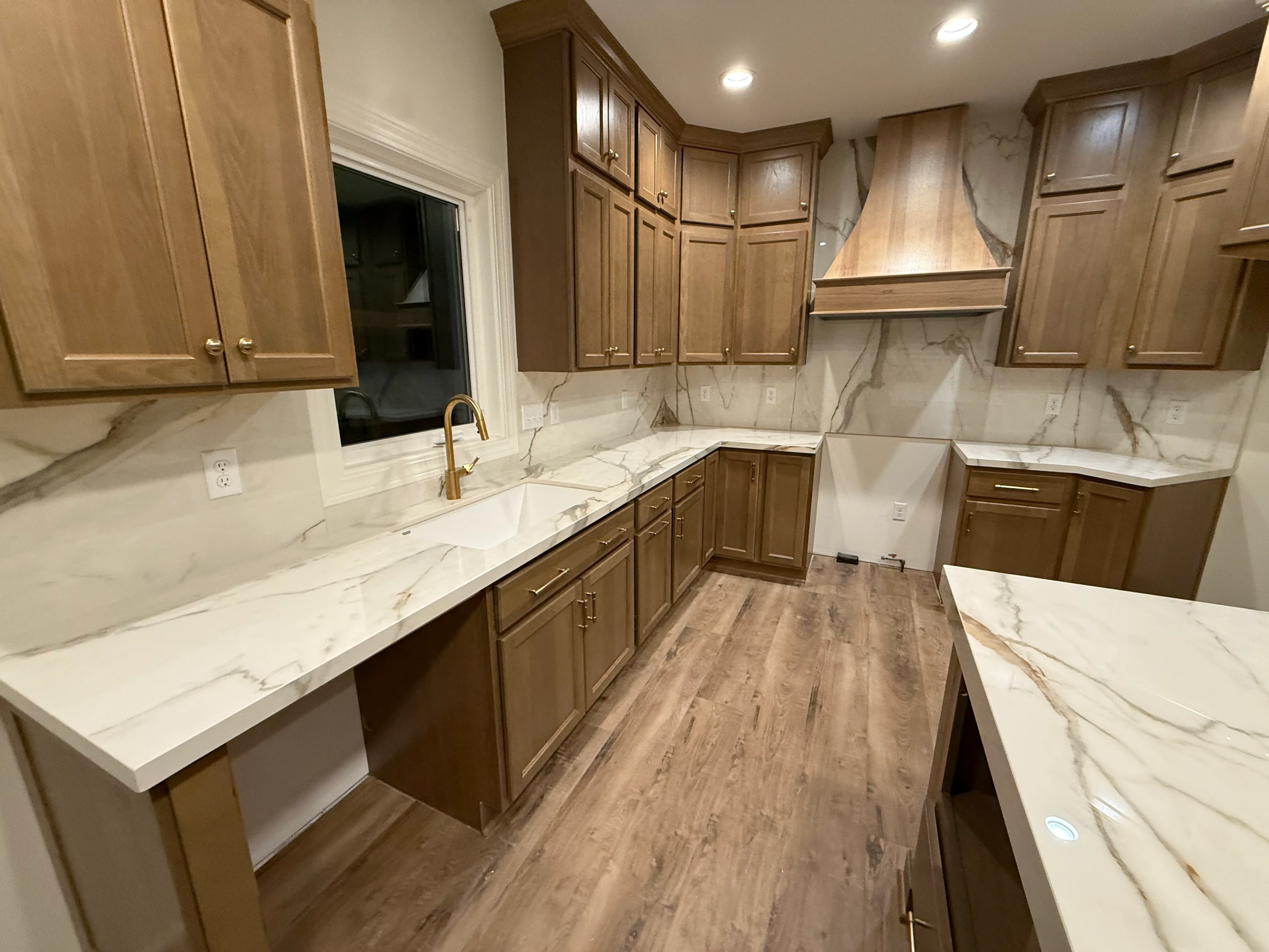 White marble countertops and backsplash with walnut cabinets and brass sink faucet
