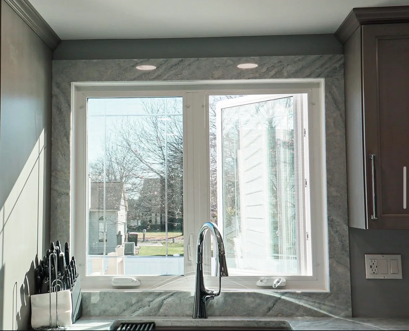 Light gray veined marble countertop and backsplash with black faucet and recessed lighting
