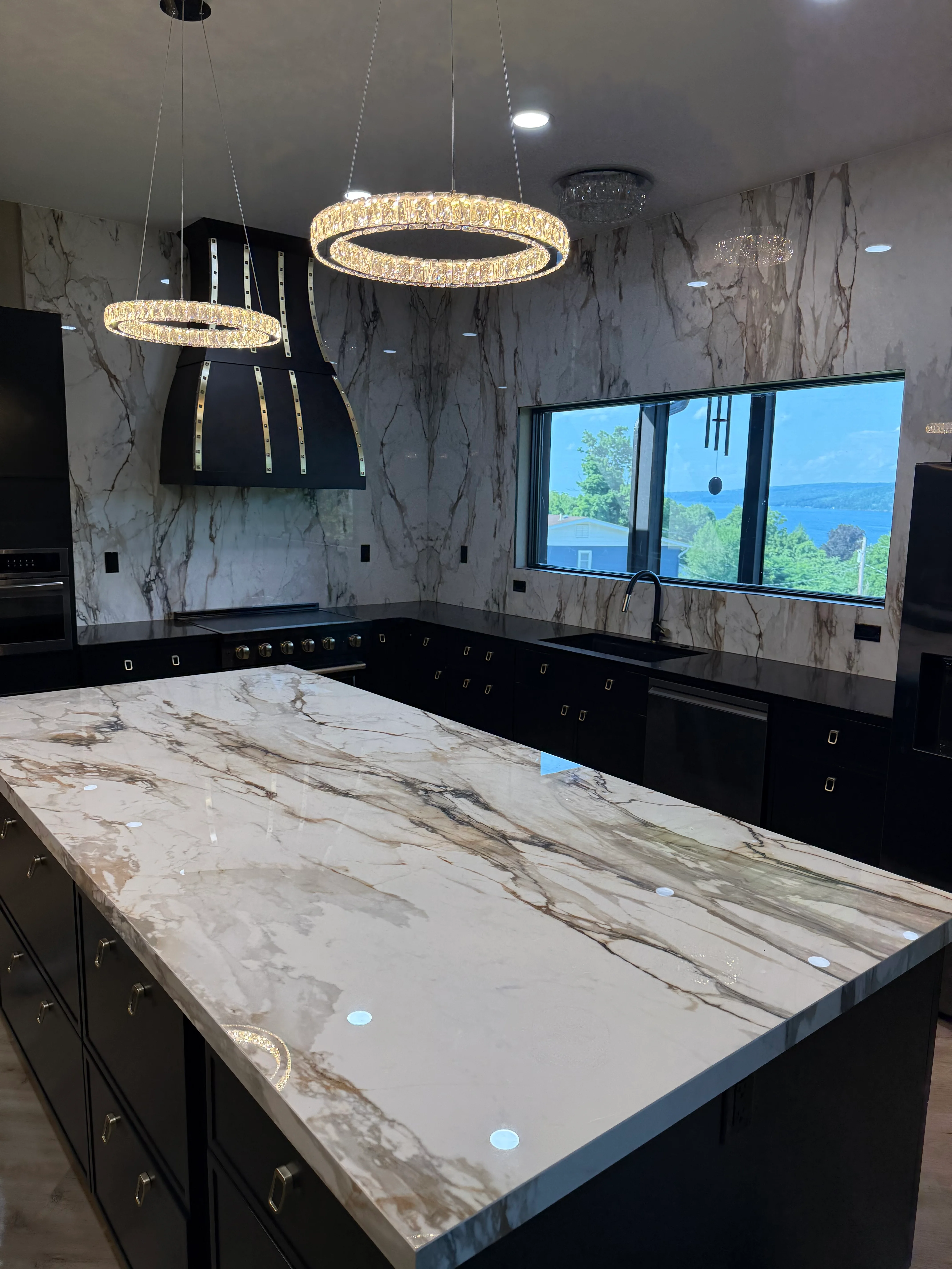 Marble countertop and backsplash installation with black cabinetry and crystal pendant lights