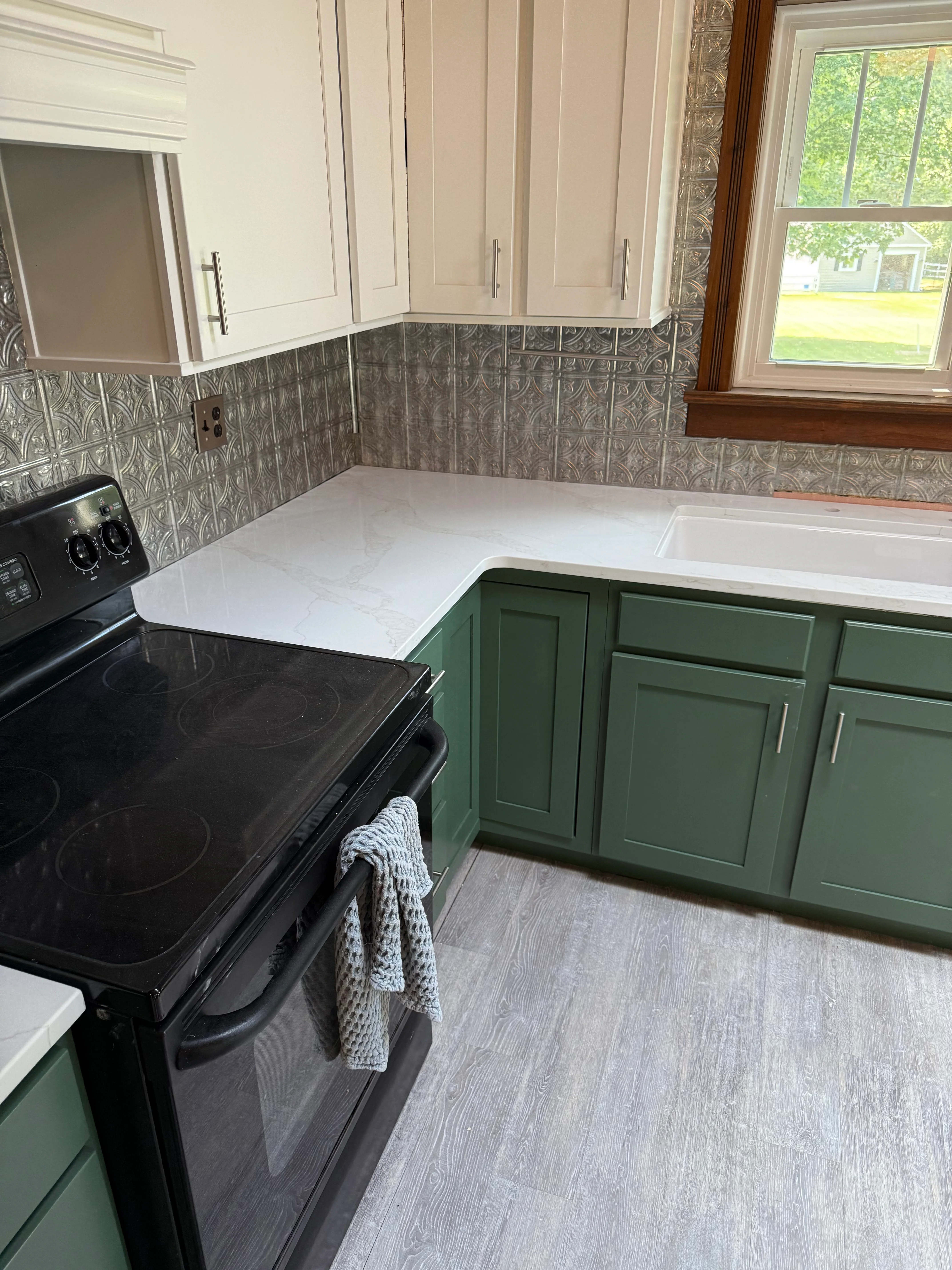 White quartz countertops with green cabinetry and embossed tin tile backsplash in kitchen