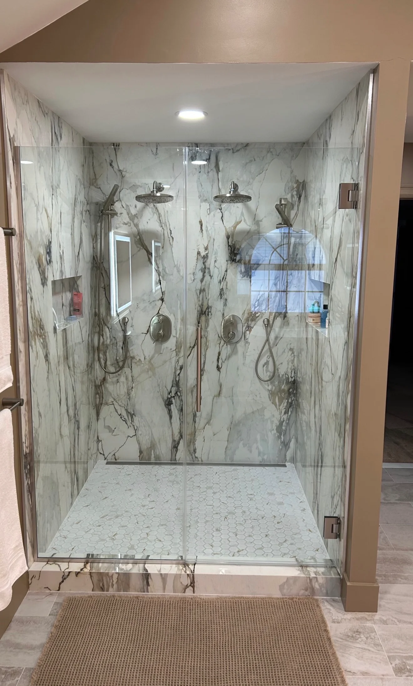 Marble shower with dual showerheads, hexagon floor tile, and frameless glass enclosure