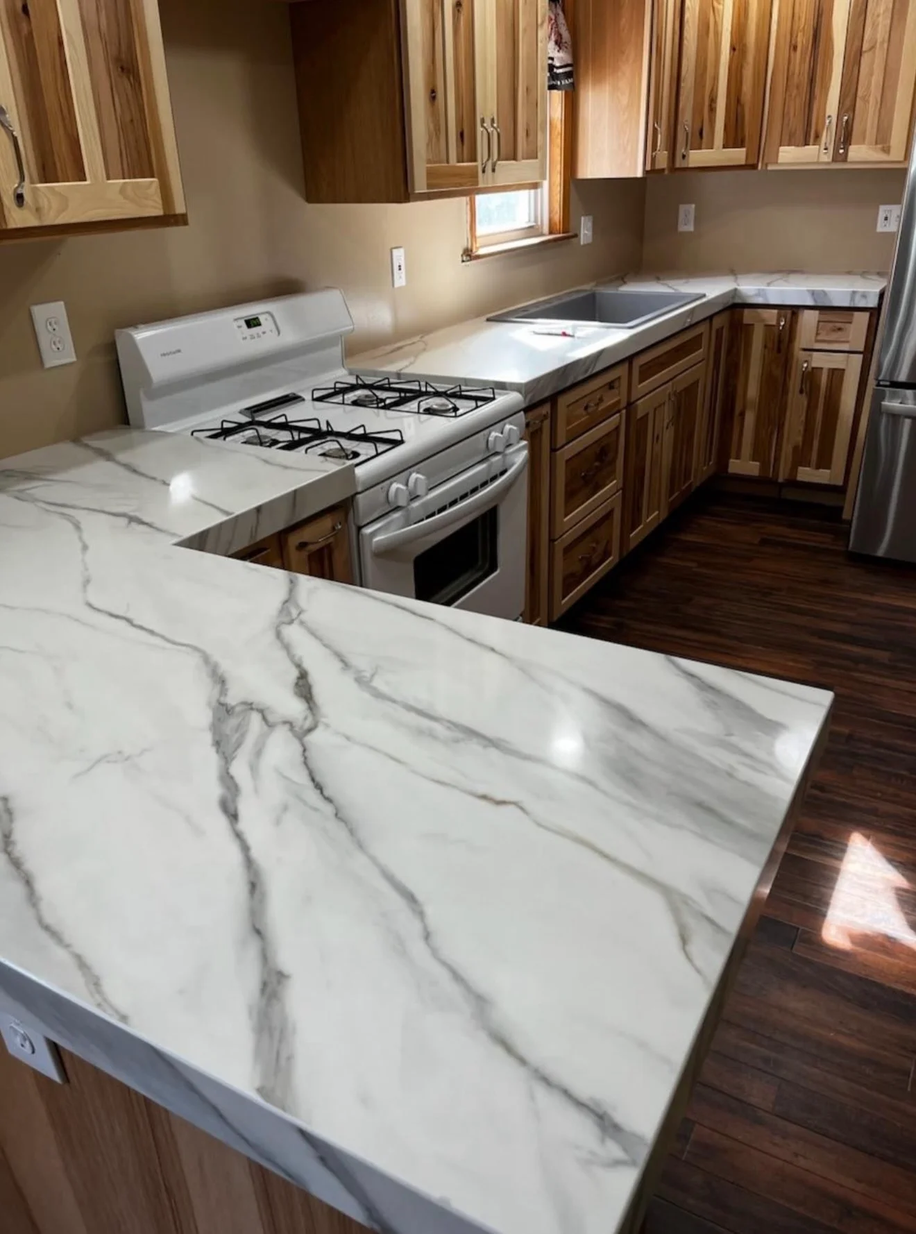 White marble countertops with gray veining installed in L-shaped kitchen with wood cabinets