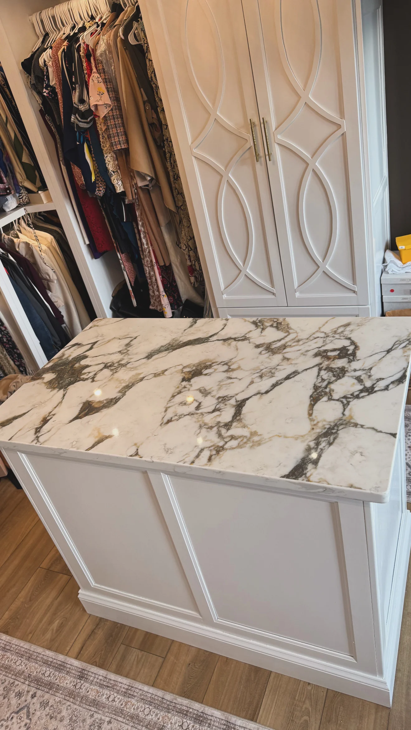 White cabinetry island with gray-veined marble countertop in closet space